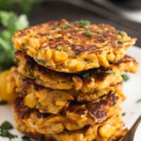 stapled zucchini and corn fritters with parsley on a plate with a fork.