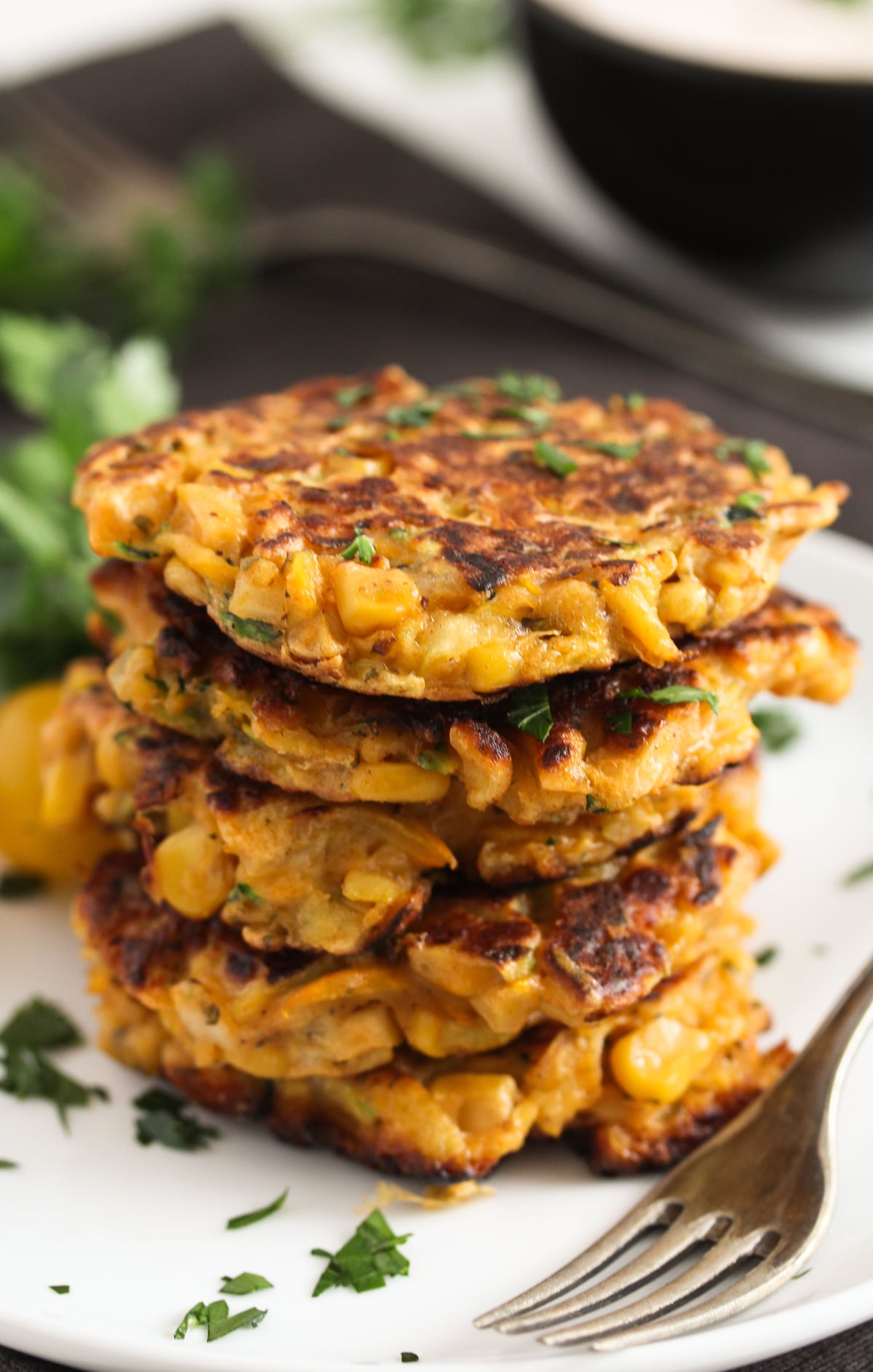 stapled zucchini and corn fritters with parsley on a plate with a fork.