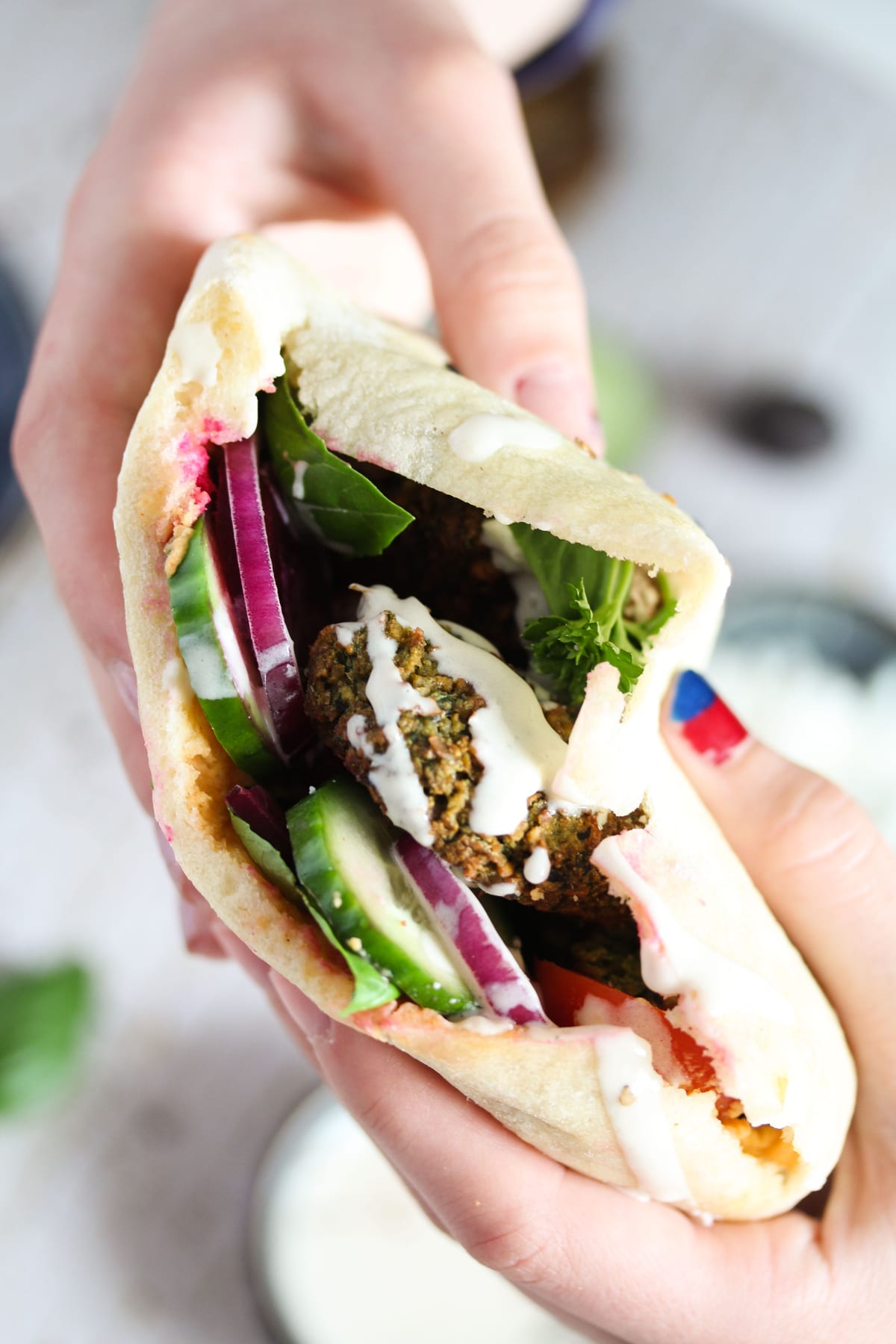 girl's hands holding a pita sandwich with chickpea balls and vegetable slices.