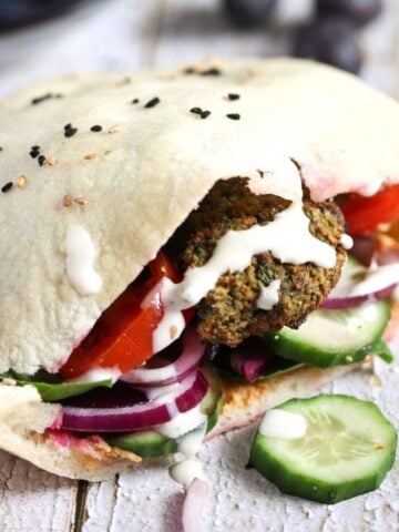 falafel sandwich with tahini and cucumber slices on a wooden table.