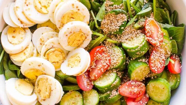 overhead view of a bowl of salad with spinach, eggs, tomatoes and cucumbers.