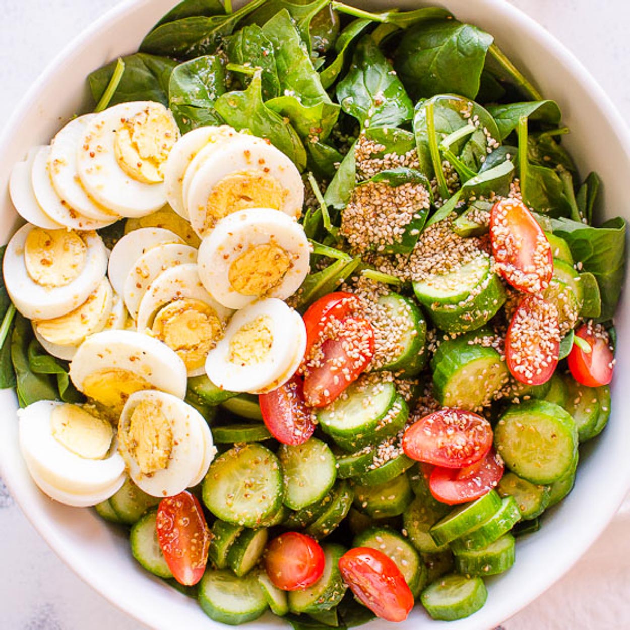 overhead view of a bowl of salad with spinach, eggs, tomatoes and cucumbers.