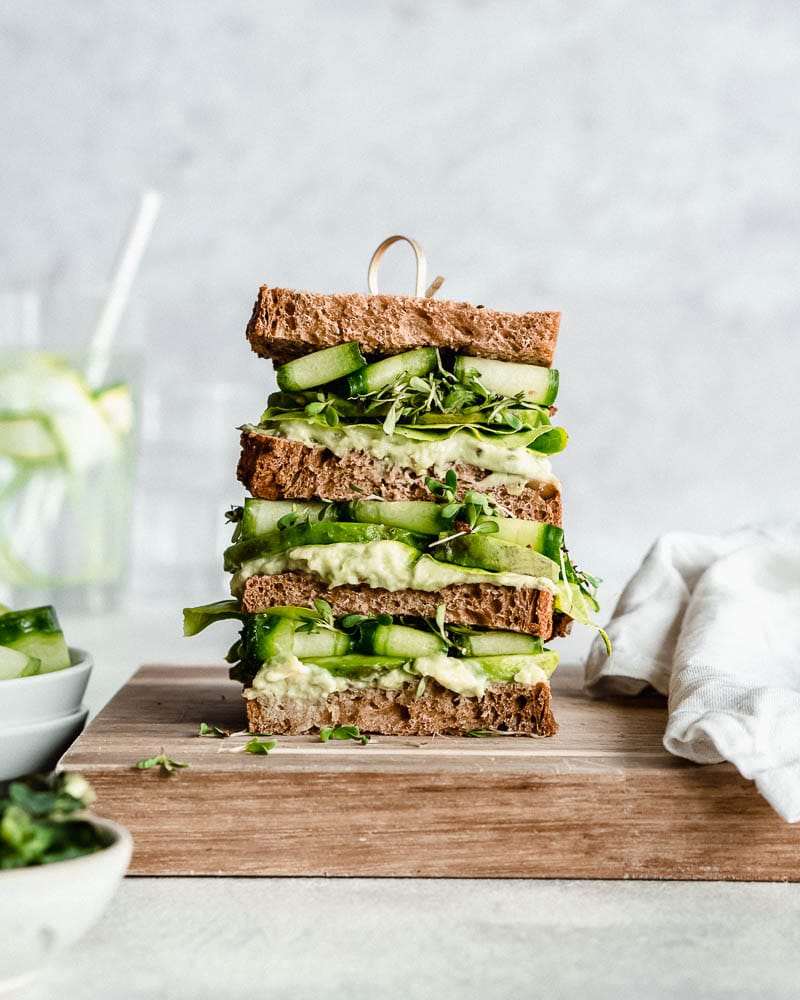 stapled green goddess avocado sandwich on a wooden board.