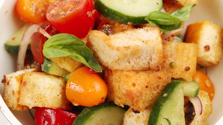 close up bowl of panzanella salad with bread, tomatoes, cucumbers and onions.