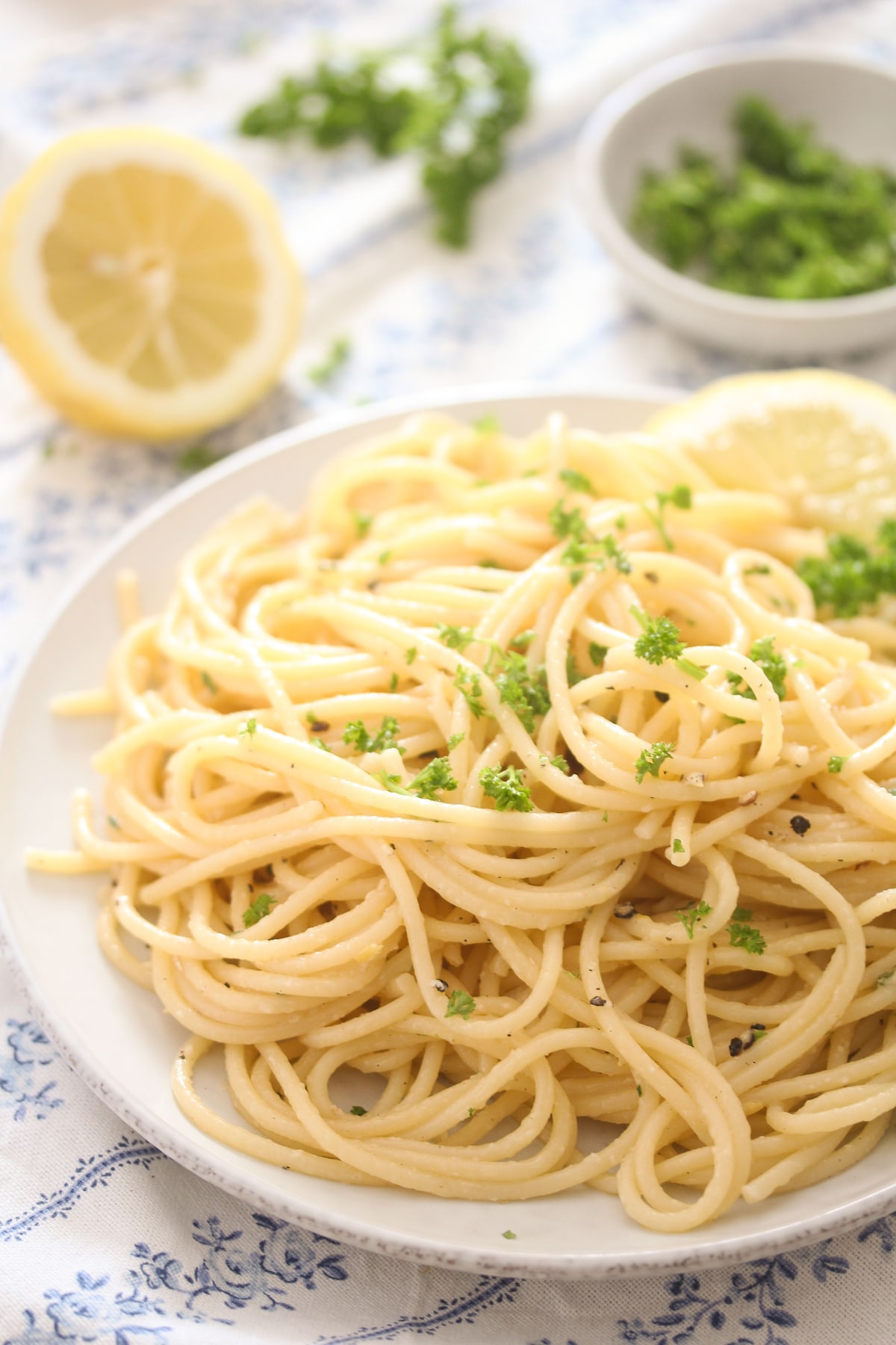 plate with a tangle of spaghetti with a halved lemon and parsley behind.
