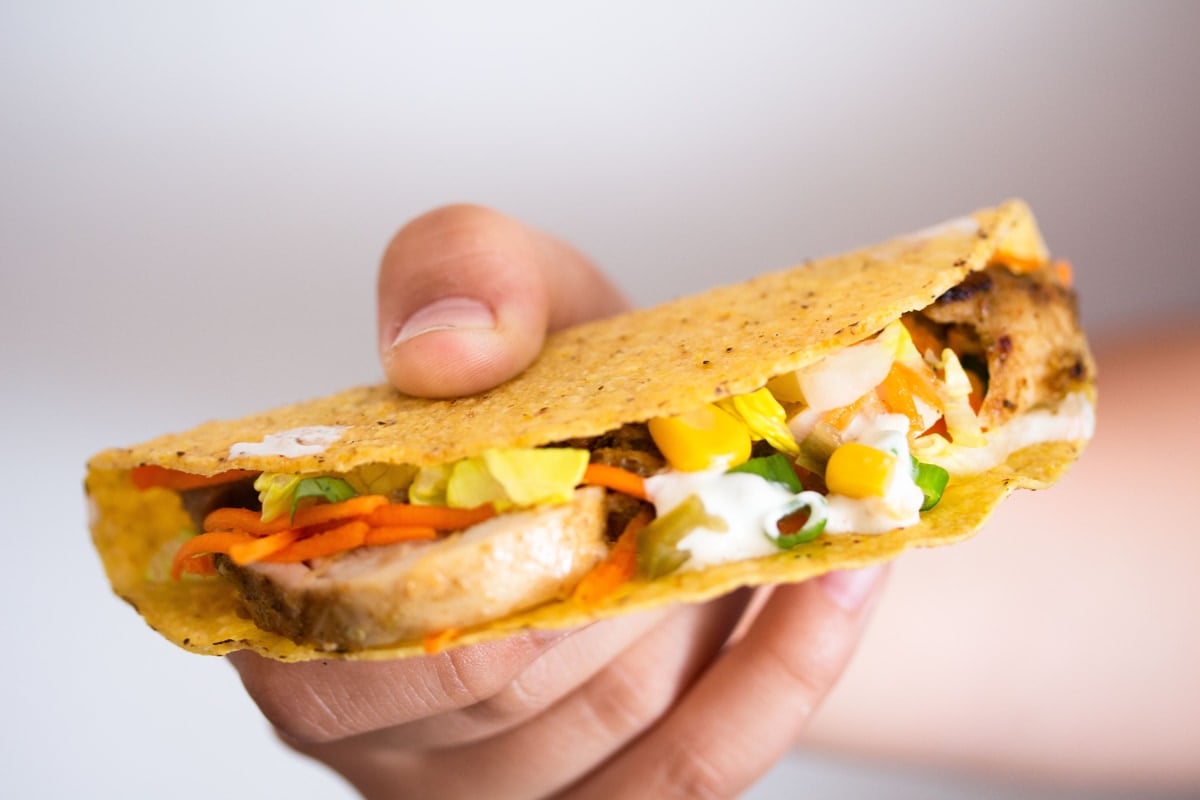 boy's hand holding a chicken crunchy shell taco showing the filling.