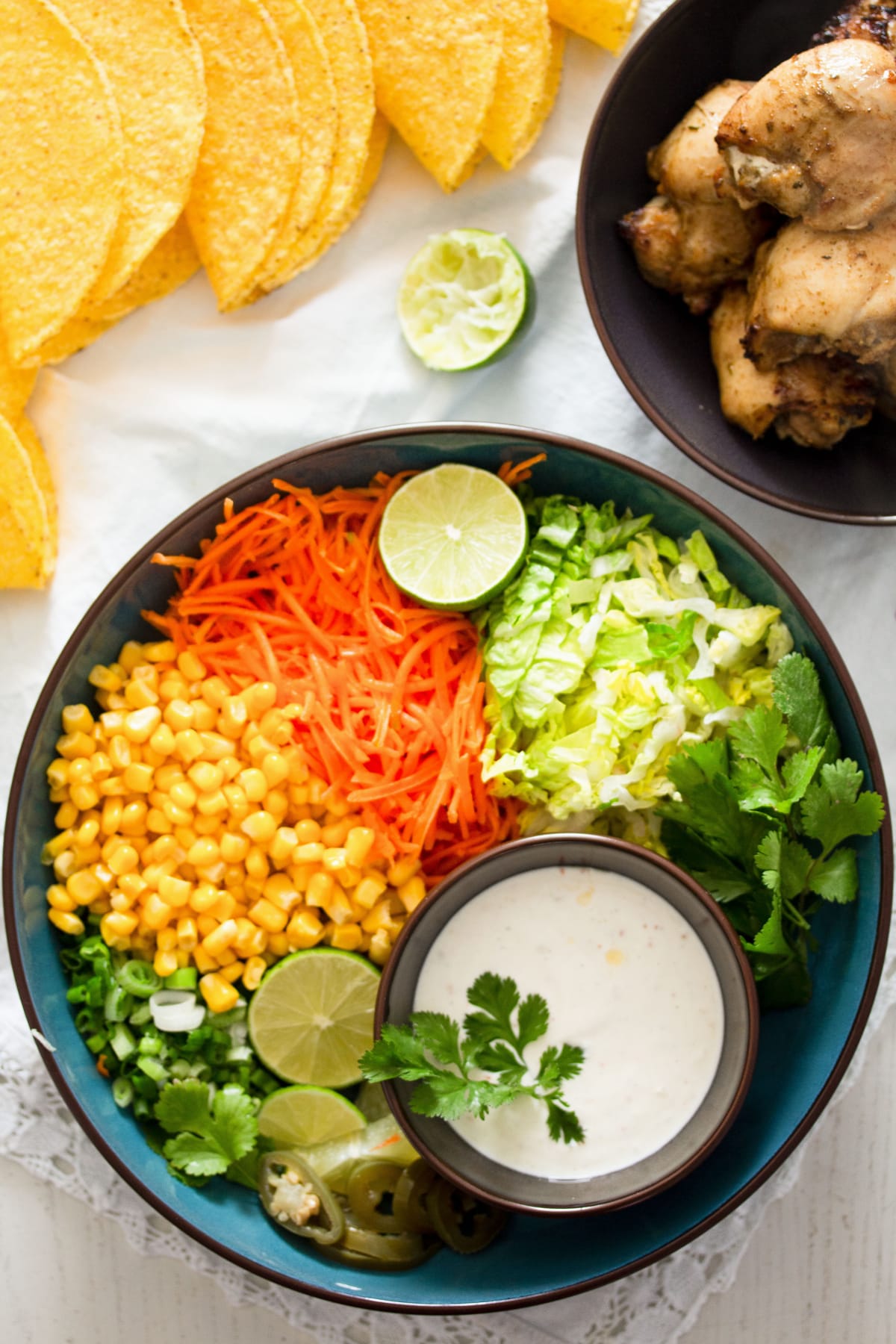 bowl with chopped vegetables and a small bowl of sauce, taco shells and chicken beside it.