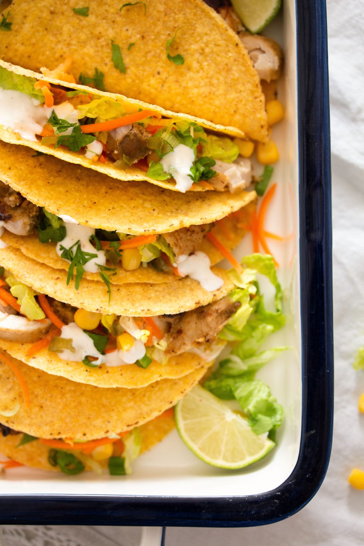 close up chicken tacos with cilantro and lime in a baking dish.