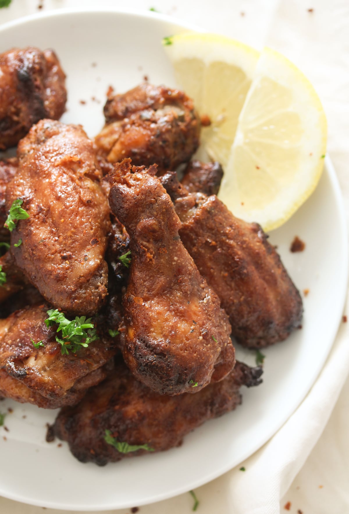 many wings with peanut butter and lemon slices on a white plate.