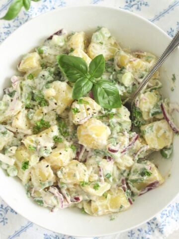 close up of spring onion potato salad in a bowl with basil on top.