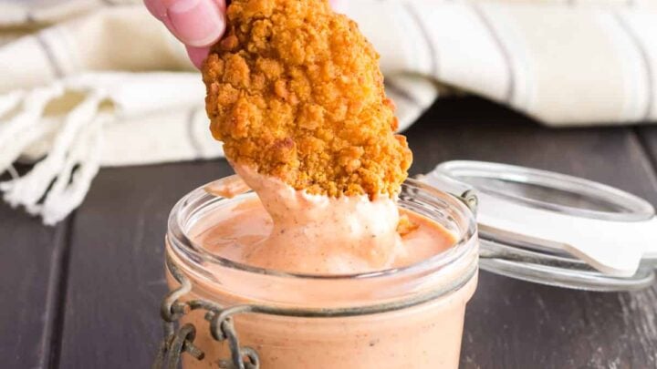 hand dipping fried food in a jar of sauce.