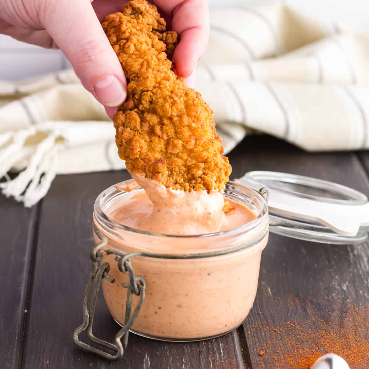 hand dipping fried food in a jar of sauce.
