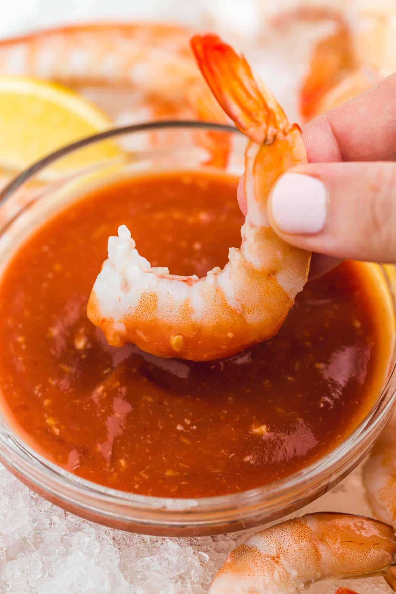 hand dipping a shrimp in cocktail sauce.