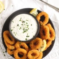 overhead view of a plate of fried breaded calamari with yogurt dip.