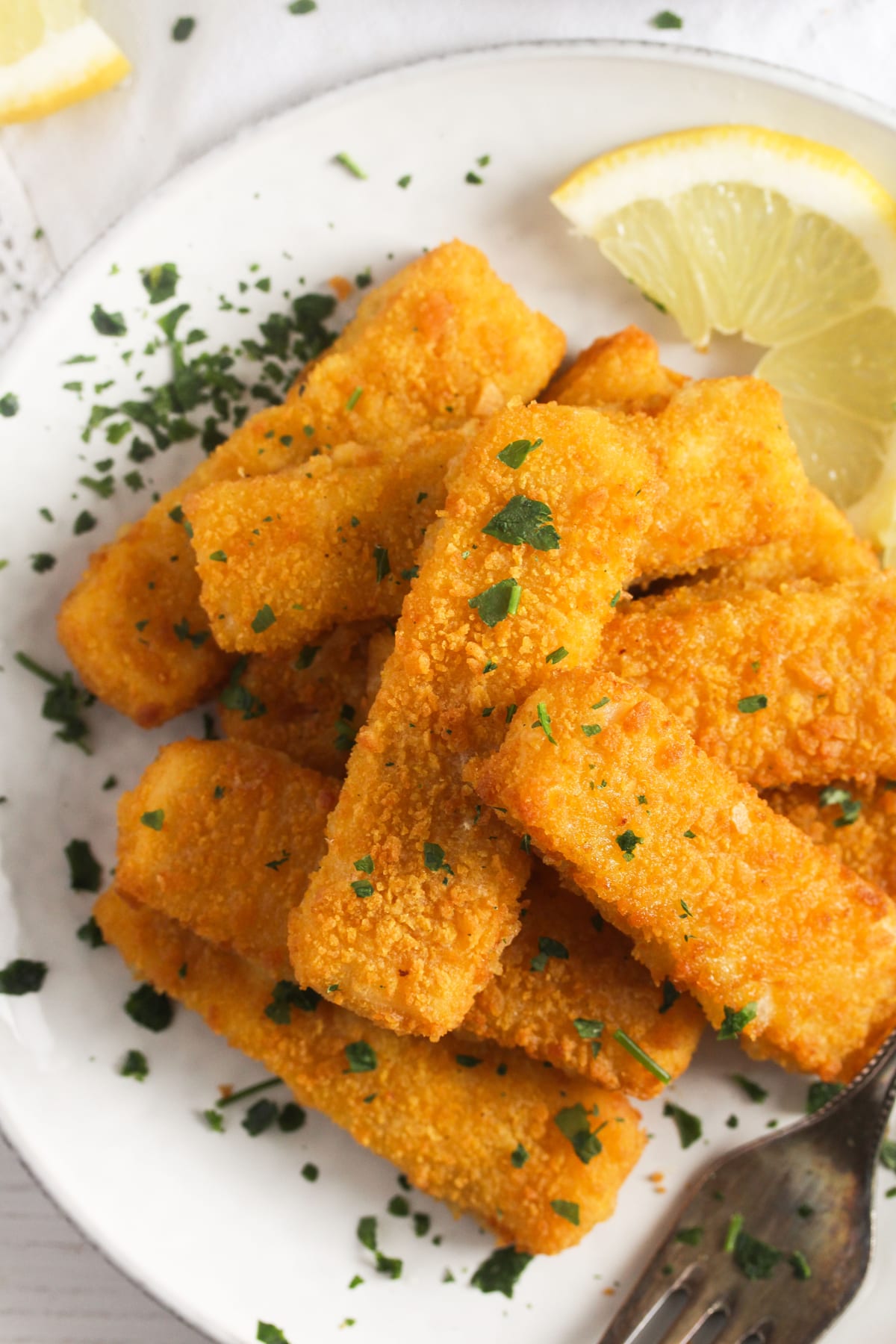 overhead view of a bunch of golden air fried fish fingers on a plate with lemons.