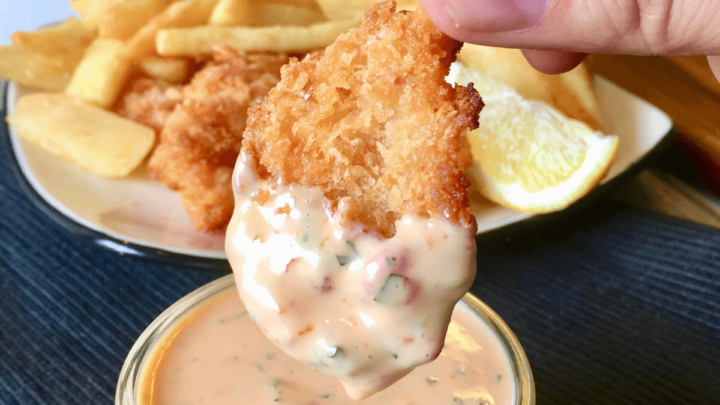 hand dipping a nugget in sweet chili sauce.