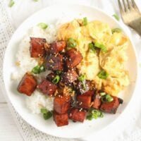 spam eggs and rice on a small white plate with a fork beside it.