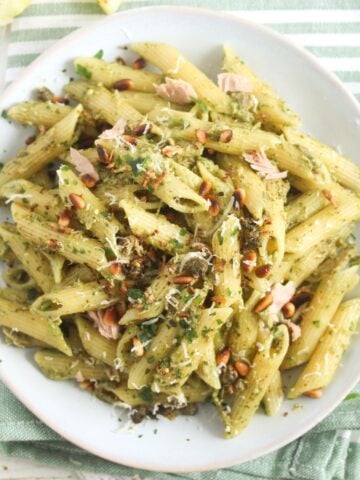 overhead view of a white plate with tuna pesto pasta sprinkled with parsley and parmesan.