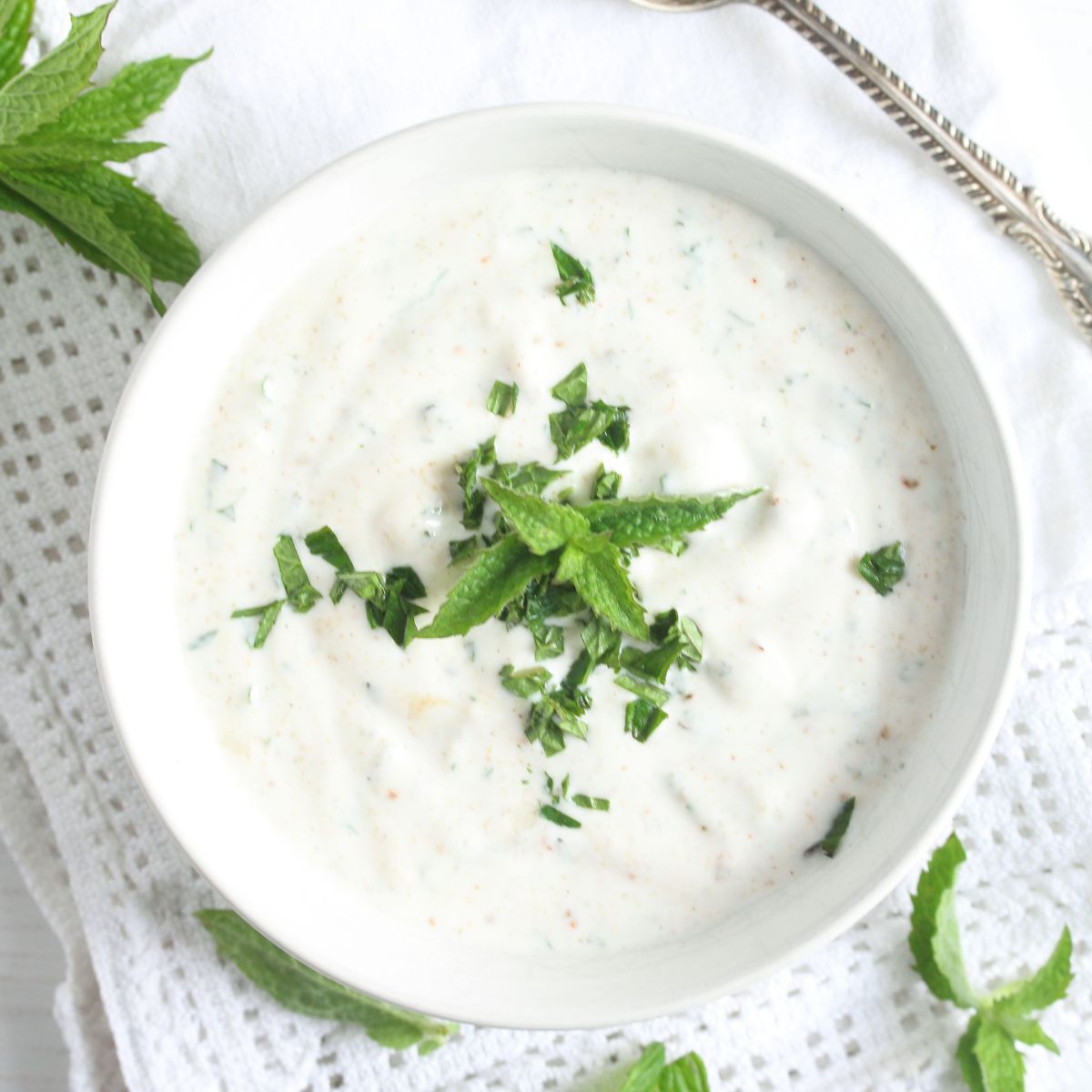 bowl with yogurt mint sauce on a white cloth.