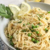 bowl with lemon ricotta pasta cooked garnished with peas, parsley and lemon wedges.