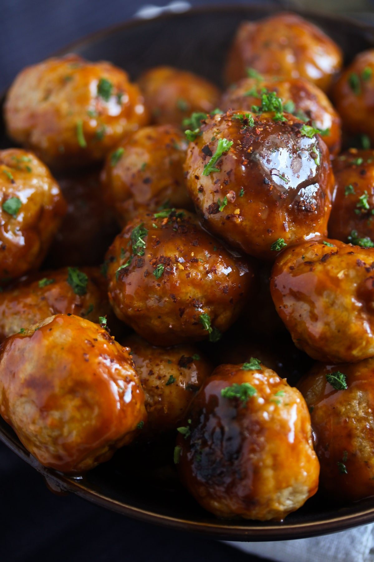 close up of many sticky meatball with turkey sprinkled with parsley.