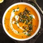 bowl of carrot pumpkin soup with a coconut milk swirl and pepitas on top.