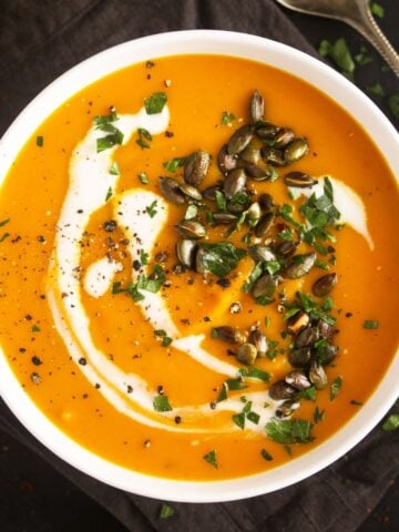 bowl of carrot pumpkin soup with a coconut milk swirl and pepitas on top.
