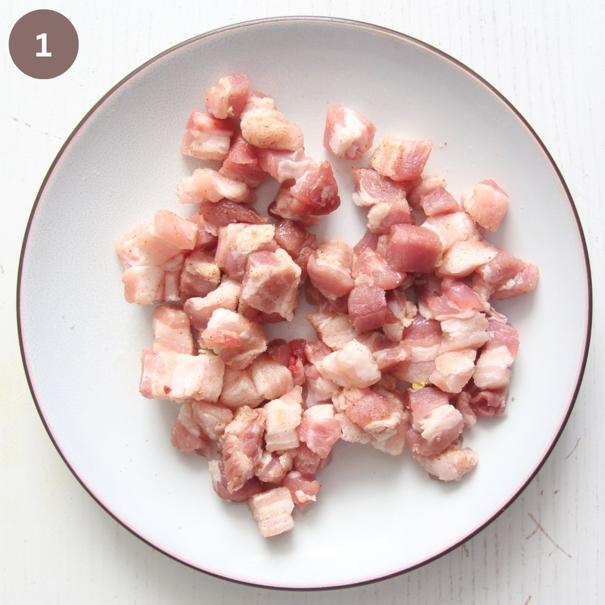 uncooked, chopped pork belly on a white plate.