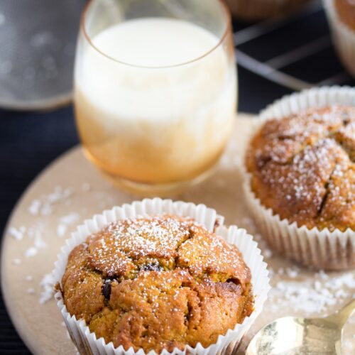 two pumpkin muffins and a small glass of milk on a round board.