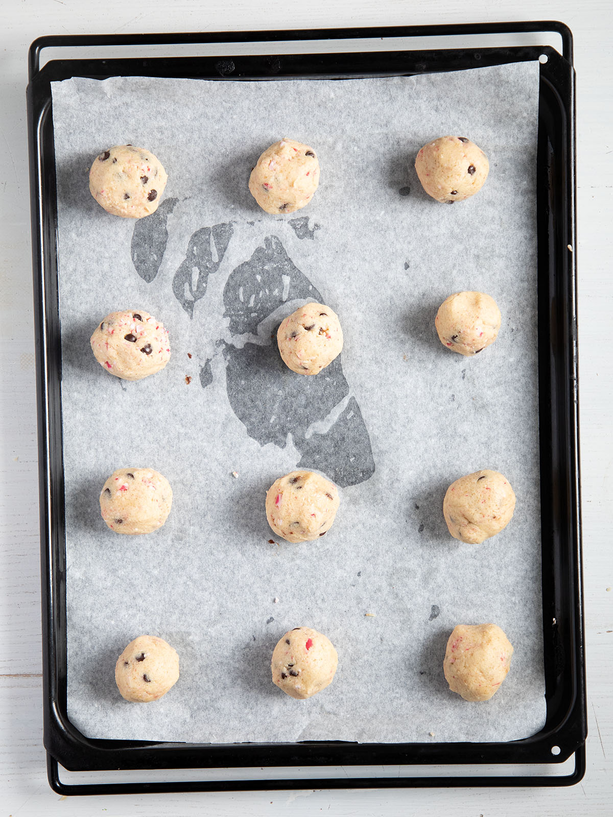12 raw cookie balls on a baking sheet lined with white parchment paper.