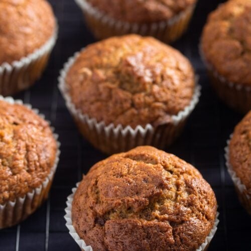 many golden brown banana pumpkin muffins on a black table.