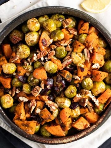 roasted sweet potatoes and brussels sprouts in a brown bowl on a white cloth.