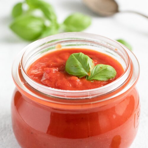 small round jar filled with italian tomato sauce with basil leaves on top.