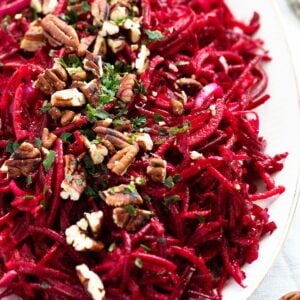 close up vibrant beet apple salad topped with pecans and parsley.