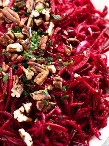 close up vibrant beet apple salad topped with pecans and parsley.