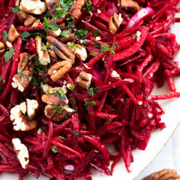 overhead view of grated beetroot and apple salad with pecan nuts and parsley on top.
