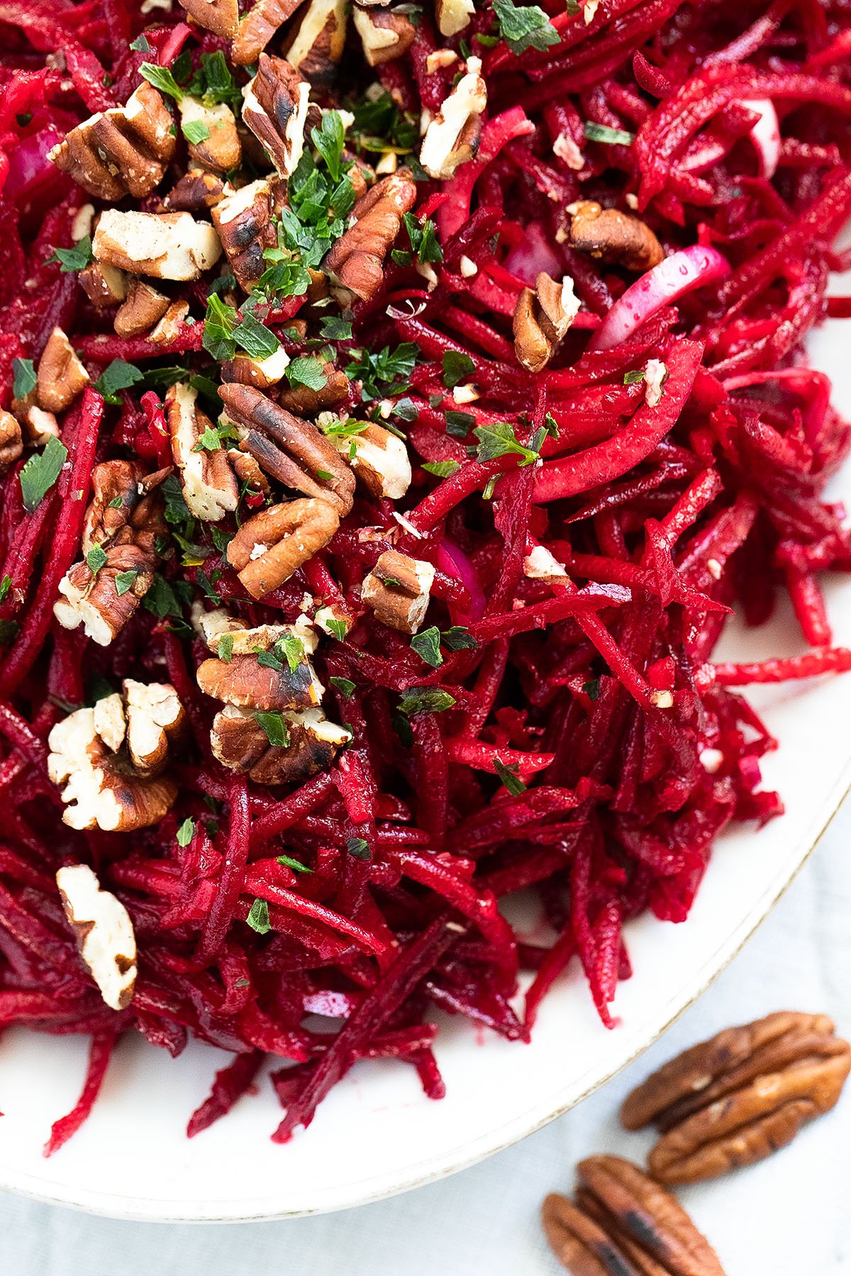 overhead view of grated beetroot and apple salad with pecan nuts and parsley on top.