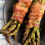 air fryer bacon wrapped asparagus on a small black plate.