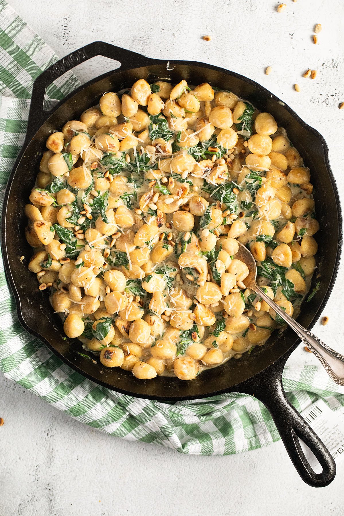 overhead view of a skillet full of gnocchi in creamy spinach sauce with a spoon in it.