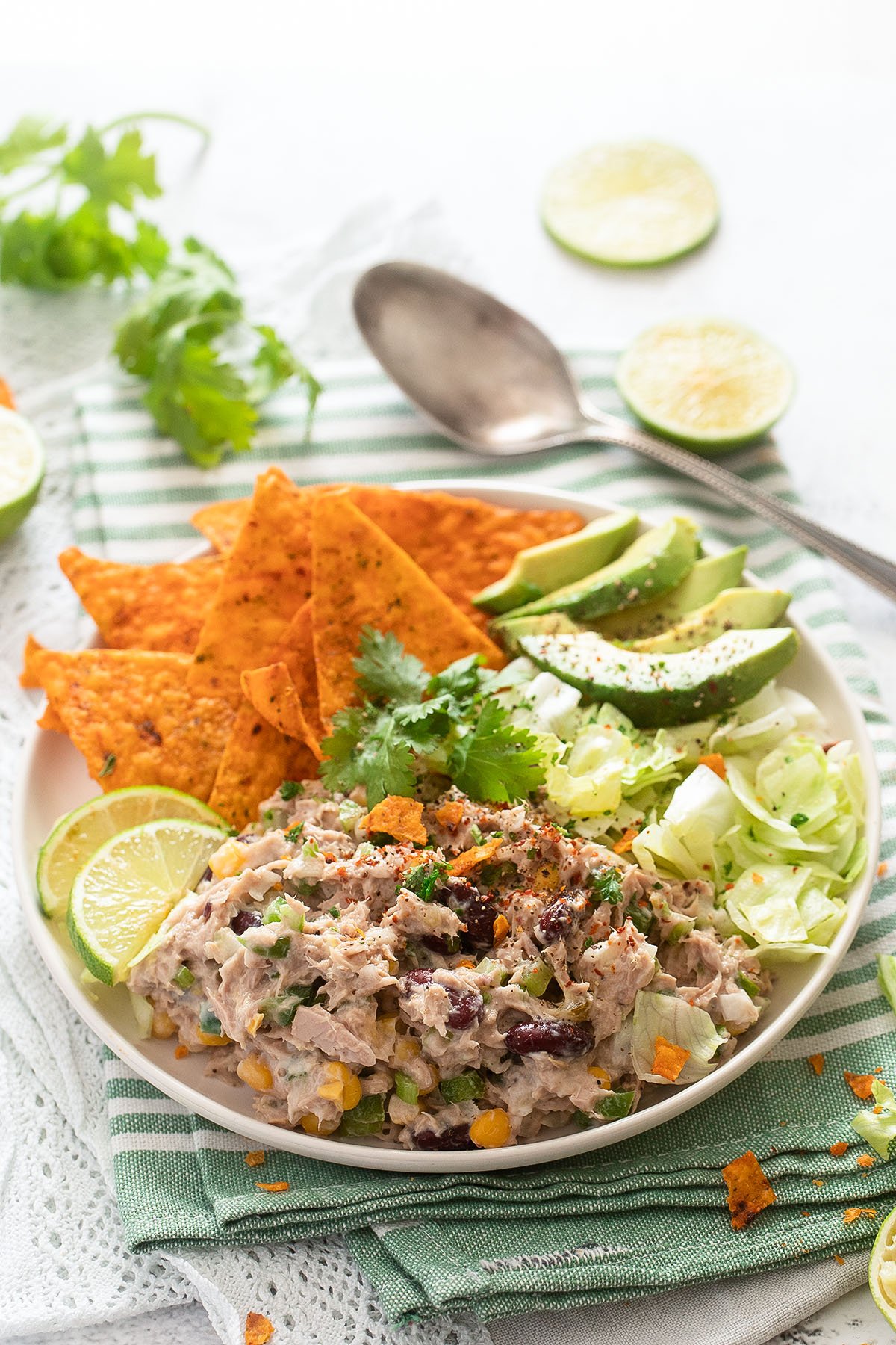plate with tuna salad with corn and beans, tortilla chips, avocado, lettuce and lime.