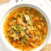 bowl of soup with carrots and celery and some bread slices around it.