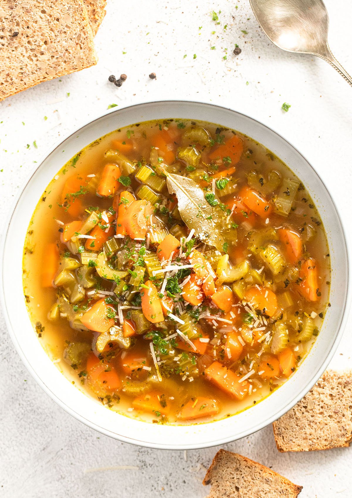 bowl of soup with carrots and celery and some bread slices around it.