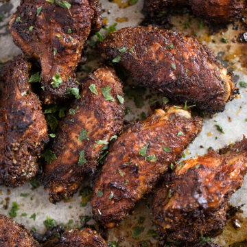 many dry rub wings sprinkled with parsley on a tray.