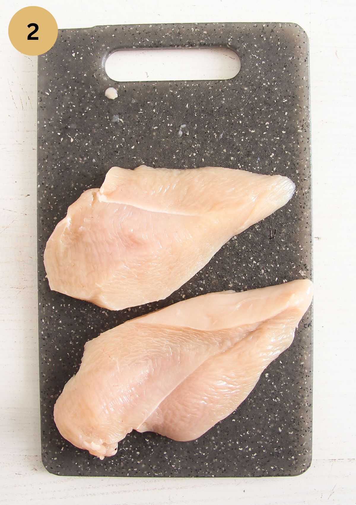 raw chicken breast sliced on a gray cutting board.