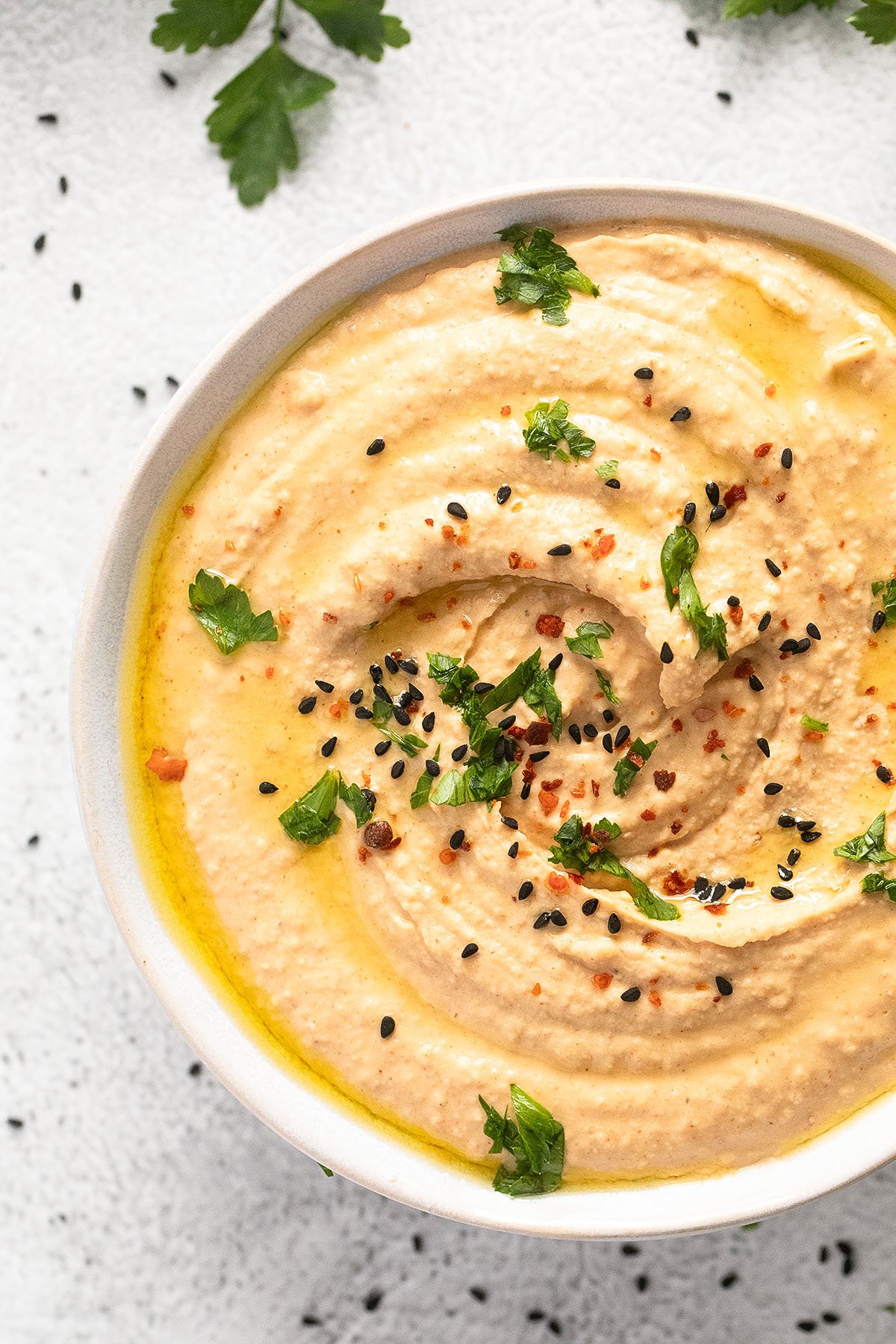 close up of a bowl of creamy hummus made with butter beans and sprinkled with nigella seeds and parsley.