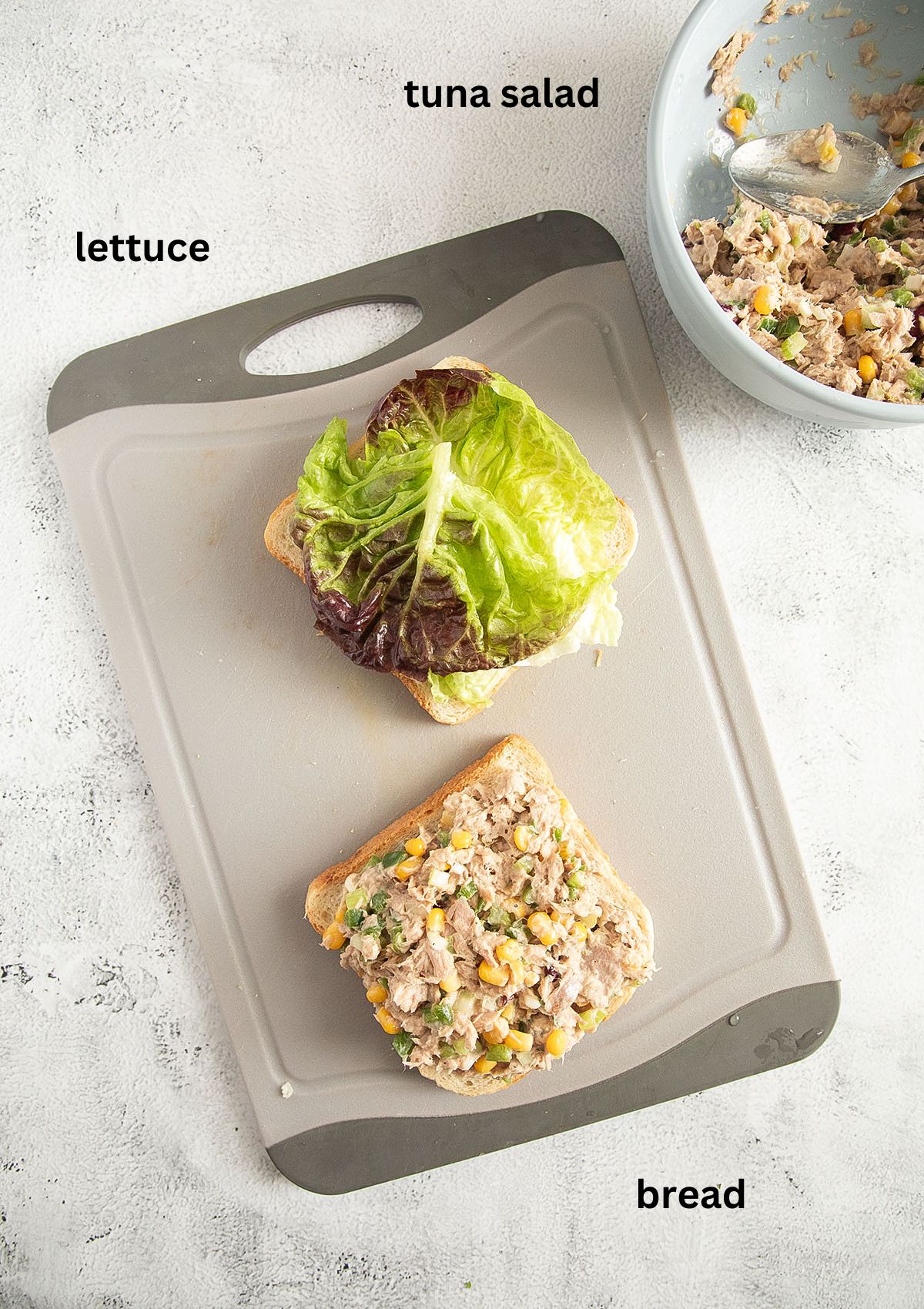 making a sandwich with tuna salad and lettuce on a cutting board.