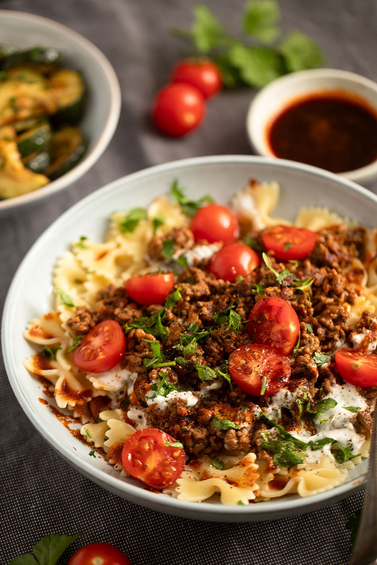 a dish with pasta topped with groun beef, yogurt sauce and cherry tomatoes.