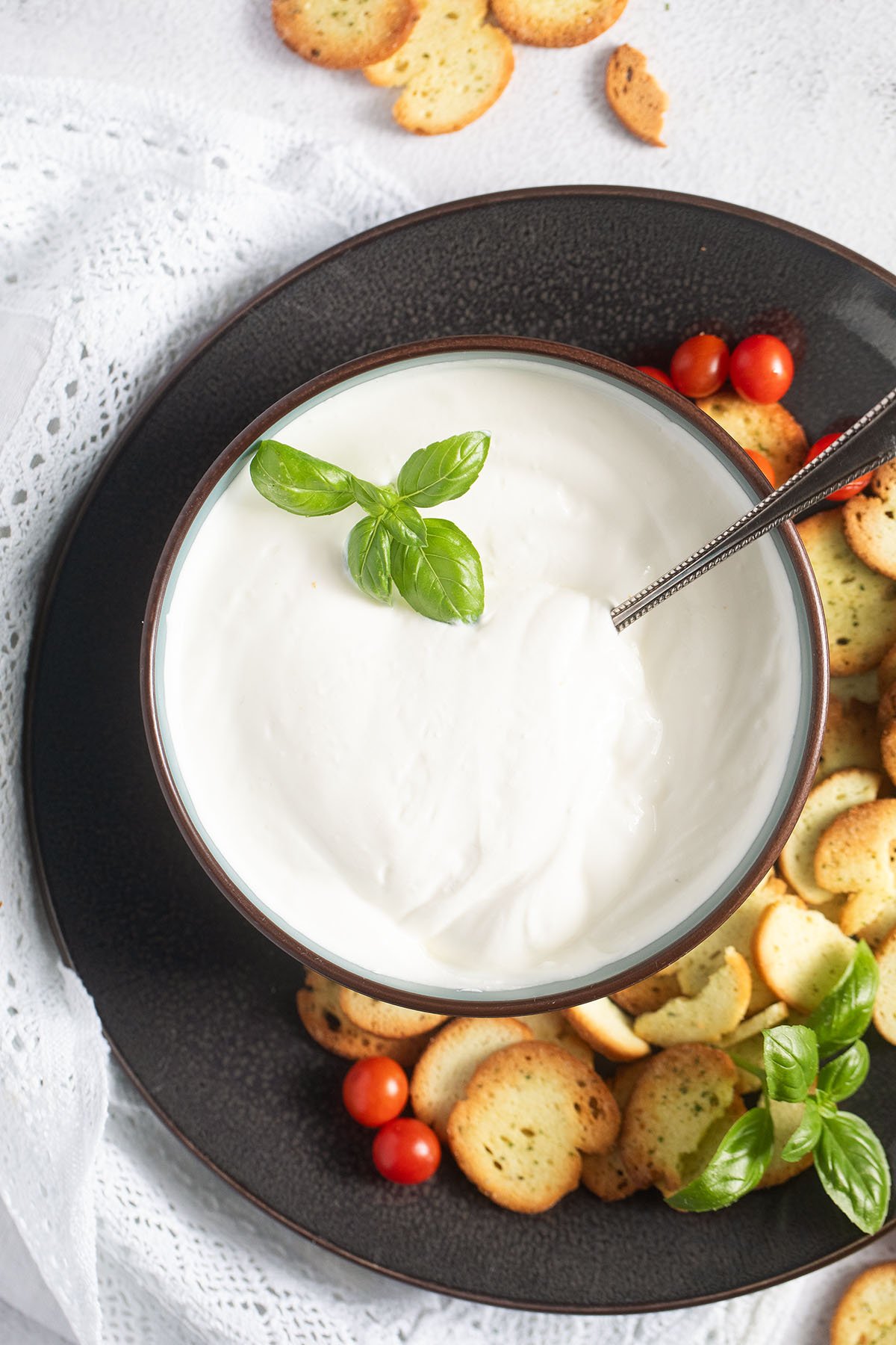 a large brown plate with a bowl of creamy cottage cheese, crackers and tomatoes on it.