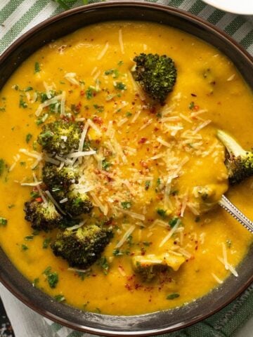 carrot and broccoli soup in a brown bowl with roasted broccoli florets in it.