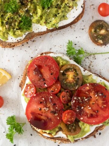 two slices of cottage cheese toast with avocado and with sliced tomatoes.